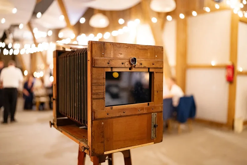 Die originale Photobooth aus Holz zwischen Gästen und warmen Lichterketten in einem Festsaal.